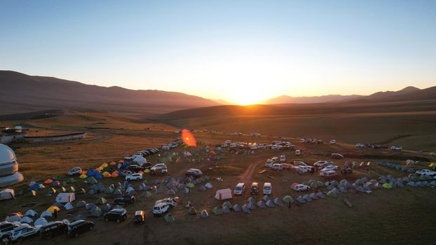 Bright dawn over the Assy-Turgen Observatory in the mountains. Aerial view from the drone of the camp of tents, cars and waking tourists. There is an old abandoned building. Kazakhstan, Almaty