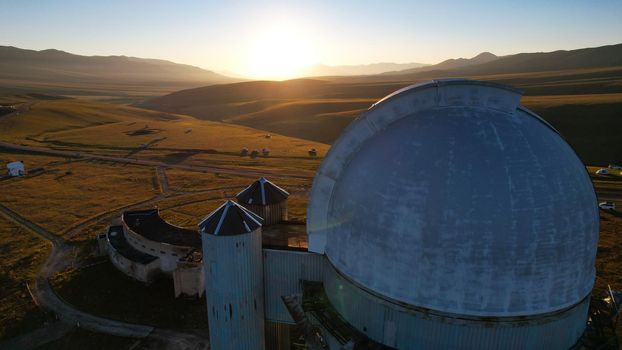 Bright dawn over the Assy-Turgen Observatory in the mountains. Aerial view from the drone of the camp of tents, cars and waking tourists. There is an old abandoned building. Kazakhstan, Almaty