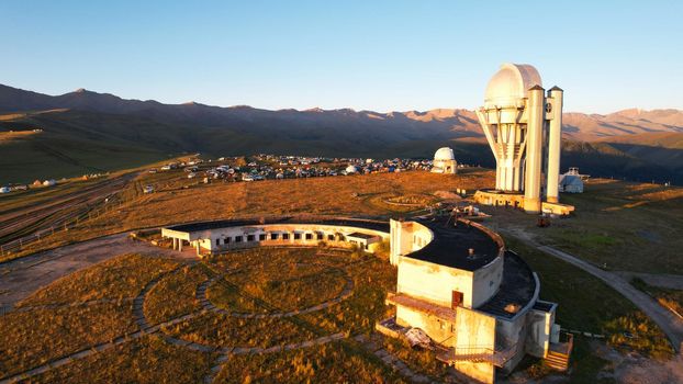 Bright dawn over the Assy-Turgen Observatory in the mountains. Aerial view from the drone of the camp of tents, cars and waking tourists. There is an old abandoned building. Kazakhstan, Almaty