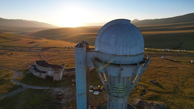 Bright dawn over the Assy-Turgen Observatory in the mountains. Aerial view from the drone of the camp of tents, cars and waking tourists. There is an old abandoned building. Kazakhstan, Almaty