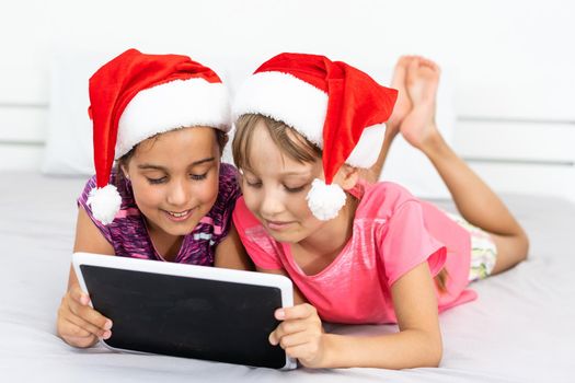 christmas, x-mas, winter, happiness concept - two adorable curly girls playing with tablet pc.