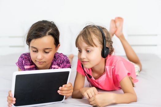 home, leisure, new technology and music concept - smiling little girl with tablet pc computer and headphones at home.