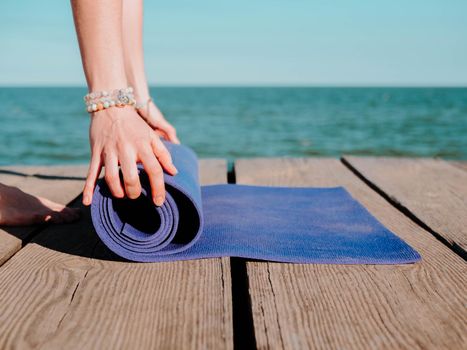 Young beautiful sporty woman preparing for yoga asana on sea beach near water. Girl covering purple mat. Health concept. High quality photo