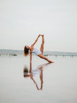 Young caucasian woman in swimsuit practicing yoga in water liman, lake or river. Beautiful reflection. Complex asanas, balance. Fitness, sport, yoga and healthy lifestyle concept. High quality photo