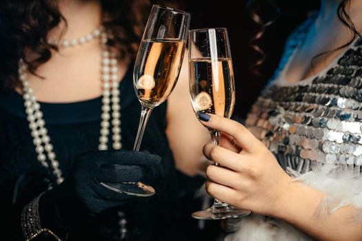 Close up glasses of champagne. Flappers women wearing in style of Roaring Gatsby twenties drinking alcohol. Vintage, retro party, fashion, girls friends concept. High quality photo