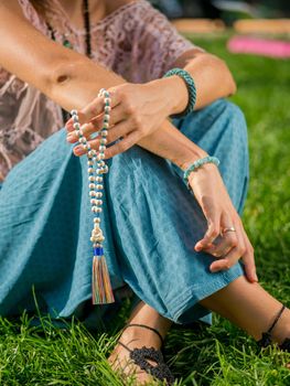 Woman, lit hand close up, counts Malas, strands of wooden beads used for keeping count during mantra meditations. Buddhism. Girl sitting in the park at summer. High quality photo