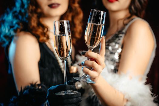 Close up glasses of champagne. Flappers women wearing in style of Roaring Gatsby twenties drinking alcohol. Vintage, retro party, fashion, girls friends concept. High quality photo