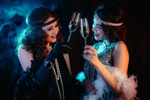 Close up glasses of champagne. Flappers women wearing in style of Roaring Gatsby twenties drinking alcohol. Vintage, retro party, fashion, girls friends concept. High quality photo