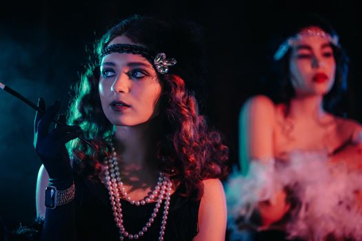 Portrait of young flapper women dressed in style of Great Gatsby posing on dark velours background. Roaring twenties, retro, party, fashion concept. High quality photo