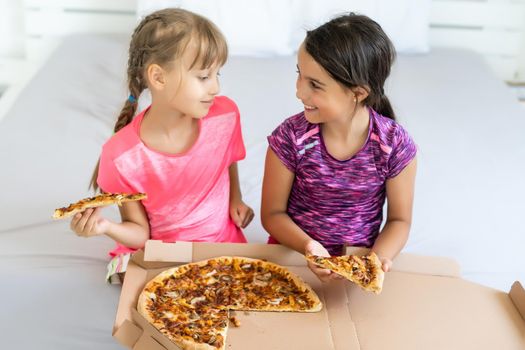 Two little girls eating pizza at home.