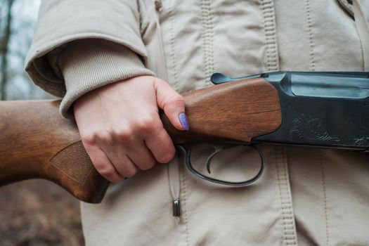 Hunter woman in warm clothes with gun. Girl hunting in the forest holding her rifle close up. High quality photo