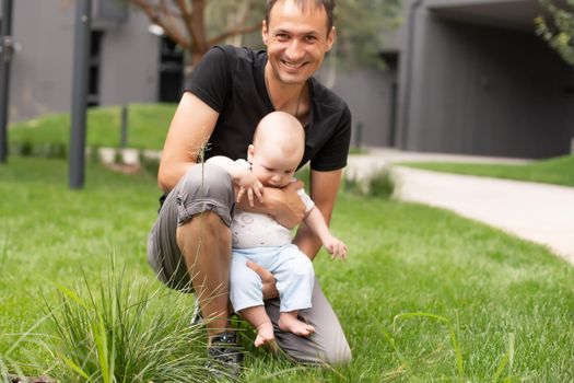 baby boy taking first steps with father help in a park.
