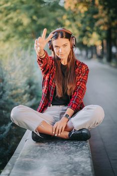 Portrait of attractive girl dancing with earphones in park. Woman smiling. moves to the rhythm.Friendly appearance of modern trendy hipster.