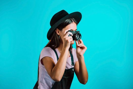 Young pretty woman in overall takes pictures with DSLR camera over blue background in studio. Girl smiling and having fun as photographer. High quality photo