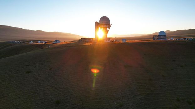 Bright dawn over the Assy-Turgen Observatory in the mountains. Aerial view from the drone of the camp of tents, cars and waking tourists. There is an old abandoned building. Kazakhstan, Almaty