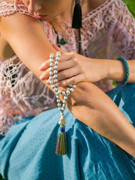 Woman, lit hand close up, counts Malas, strands of wooden beads used for keeping count during mantra meditations. Buddhism. Girl sitting in the park at summer. High quality photo