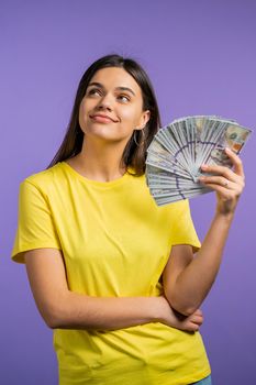 Smiling happy woman with cash money - USD currency dollars banknotes on violet wall. Symbol of jackpot, gain, victory, winning the lottery.