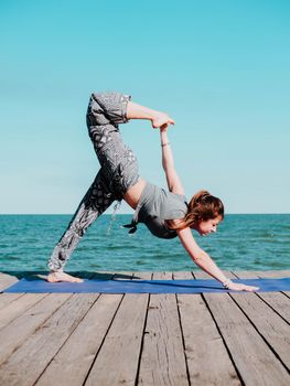 Young beautiful sporty woman in comfortable clothing doing yoga asana on sea beach near water. Girl practicing exercises. Health concept. Colorful picture. High quality photo