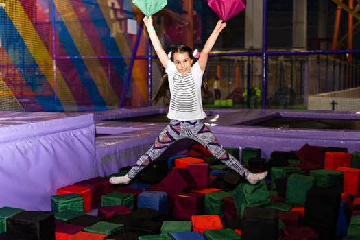 Portrait little cute child girl playing and jumping on trampoline in children's playroom, indoors playground. Active girl having fun at sport centre