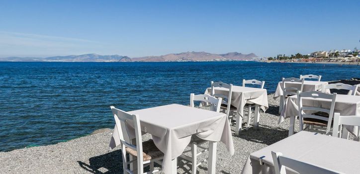 White restaurant tables on the beach in summer - travel, vacation and summer concept. The perfect lunch with a sea view