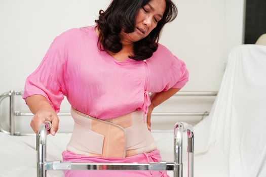 Asian senior pain back wearing elastic support belt with walker.