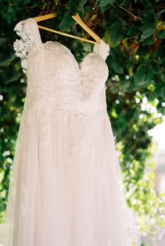 Wedding dress hanging on a wooden hanger under a tree. High quality photo