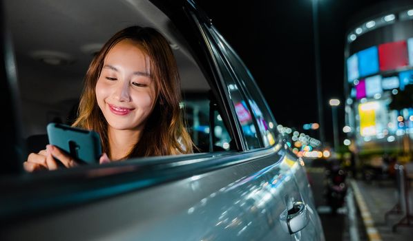 Happy beautiful woman texting smartphone sitting back seat her car in urban, Asian businesswoman commuting from office in Taxi backseat with mobile phone on road in city at night after late work