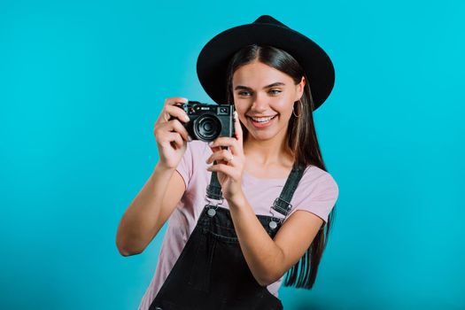 Young pretty woman in overall takes pictures with DSLR camera over blue background in studio. Girl smiling and having fun as photographer. High quality photo