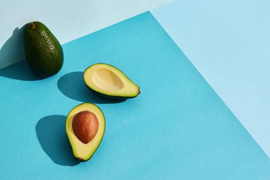 Composition of fresh fruits, whole avocado and two halfs of cutted avocado on blue background. Mock up, two-colored pastel