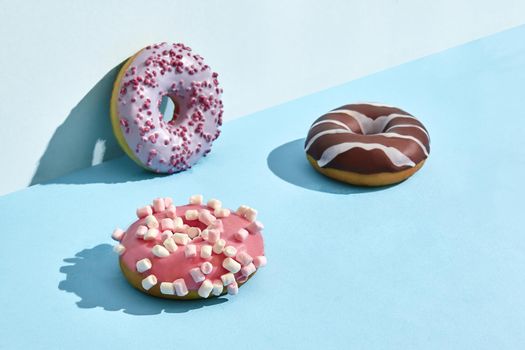 Close up photo of three sweet tasty donuts in caramel and chocolate icing, on a blue background. Mock up, two-colored pastel