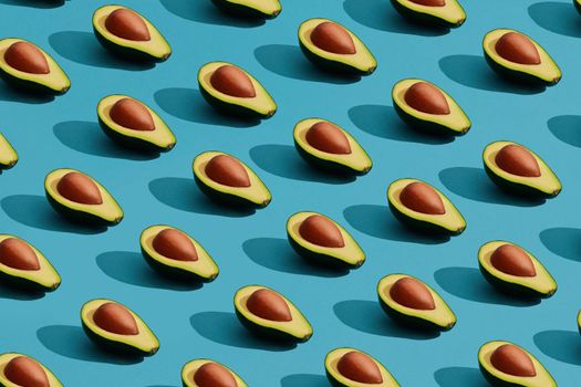 Food design. Colorful fruit pattern of fresh cutted avocado halves with pits inside on blue pastel background. Mock up, flat lay style.