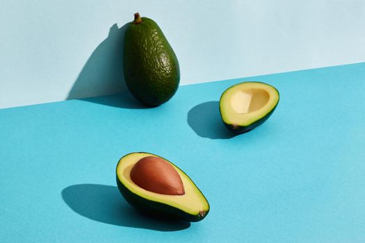 Composition of fresh fruits, whole avocado and two halfs of cutted avocado on blue background. Mock up, two-colored pastel