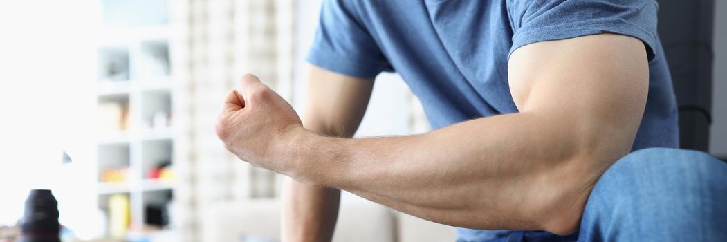 Man bending his arm and straining his biceps closeup. Home sports training concept