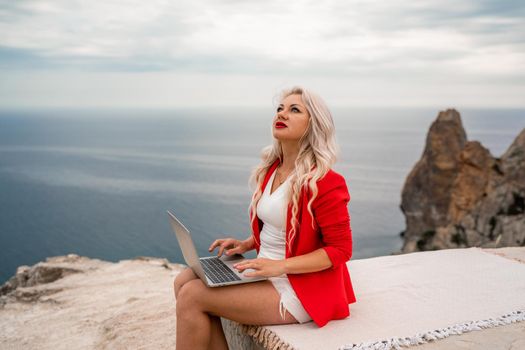 A woman is typing on a laptop keyboard on a terrace with a beautiful sea view. Freelancing, digital nomad, travel and vacation concept