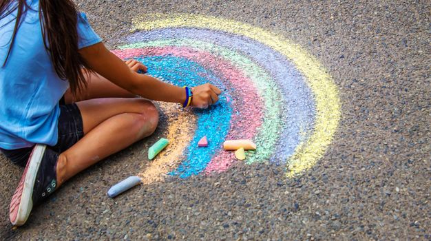 A child draws a rainbow on the asphalt. Selective focus. kid.