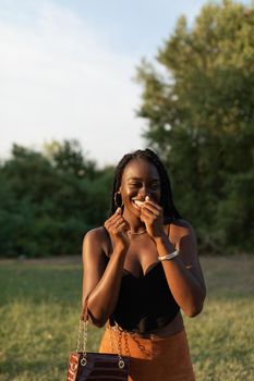 Young black female laughing embarrassingly while holding her purse at the park during a photo shoot at sunset