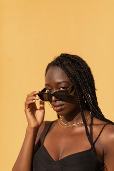 Close-up portrait of a young black woman looking at camera with expressive gaze over glasses during sunset