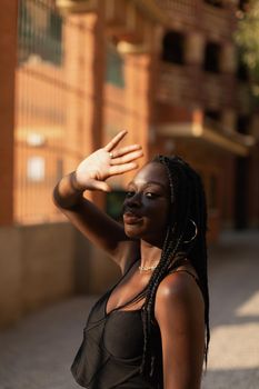 Close-up portrait of a young black woman blocking sunlight from her face with her hand in the street during sunset
