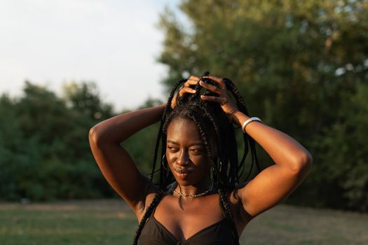 Portrait of a young black female holding her braids in a ponytail at the park during a summer sunset