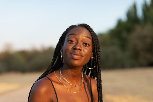 Close-up portrait of a young black female expressively looking at camera in the park during sunset