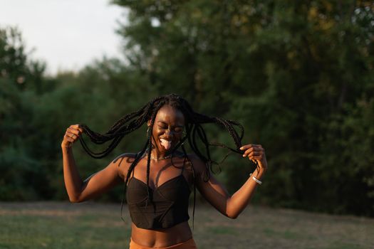 Portrait of a young black female playfuly moving her braids while sticking out her tongue at the park during sunset