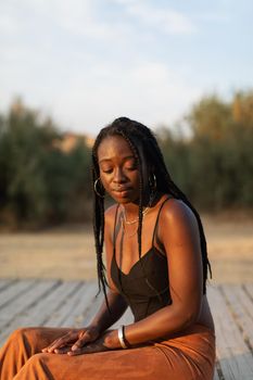 Portrait of a young black female sitting and relaxing in the park during a beautiful summer sunset