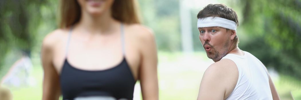 Fat man looking at young woman athlete jogging in park. Morning jogging healthy lifestyle concept