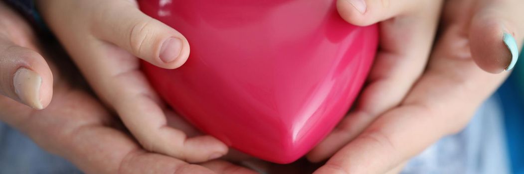 Woman and child hands holding red toy heart closeup. Save child life concept