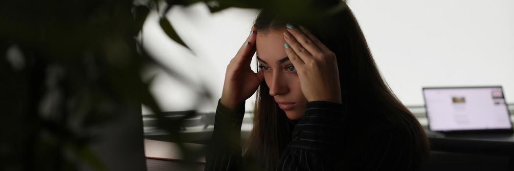 Tired woman holding her head with hands in front of computer screen in office. Headache when working at computer for long time concept