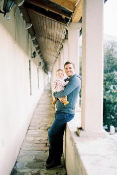Smiling dad with a baby in his arms stands on the terrace leaning against a stone fence. High quality photo