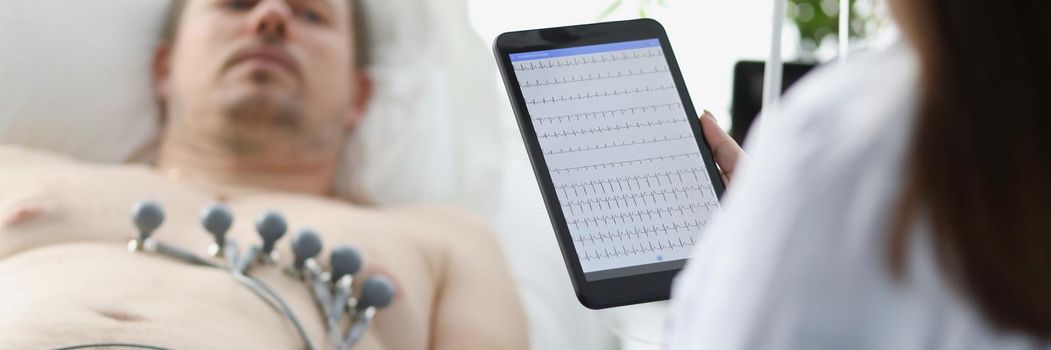 Doctor taking cardiogram to patient on couch in clinic closeup. Holter monitoring concept