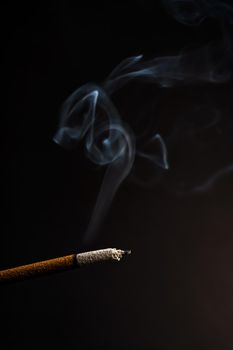 close-up of a burning incense with white smoke coming out illuminated on a black background
