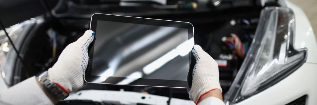 Master repairman holding digital tablet near open hood of car closeup. Modern car breakdown diagnostics concept