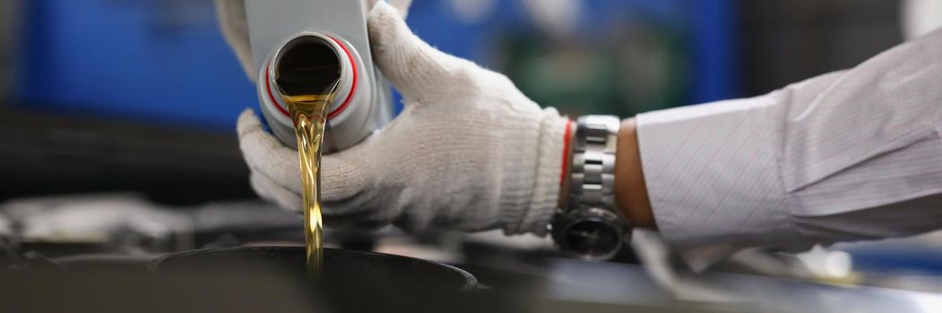 Master repairman pouring engine oil under hood of car closeup. Motor oil change interval concept